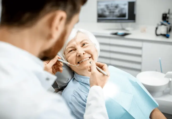 Un dentista esamina i denti di un'anziana sorridente, sottolineando l'importanza dell'igiene orale per gli anziani.