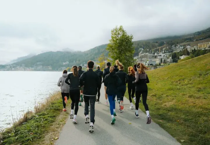 Grupa biegaczy w malowniczej scenerii nad jeziorem. Widok z tyłu na ludzi w sportowych strojach, którzy biegną ścieżką. To inspiracja, jak polubić bieganie.