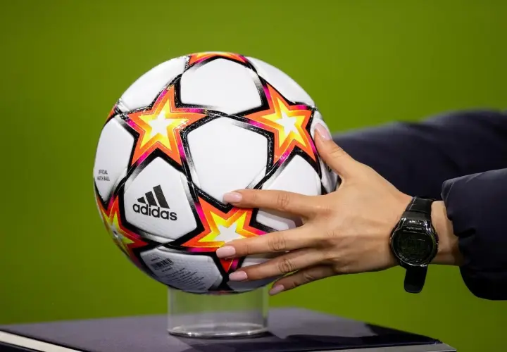 Dłoń z zegarkiem trzyma piłkę Adidas z gwiazdami, gotową do gry w ulubionym klubie piłkarskim na boisku.