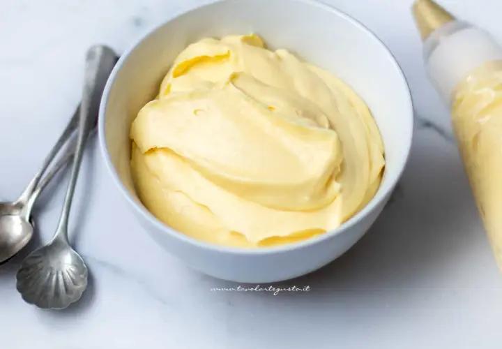 Crema pasticcera con panna, soffice e vellutata, pronta per farcire dolci. Accanto, cucchiaini d'argento e sac à poche.