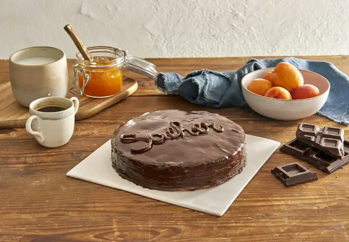 Una deliziosa torta Sacher, lucida e ricoperta di cioccolato, pronta per essere gustata con caffè, albicocche e cioccolato fondente.