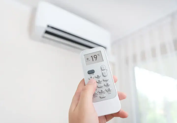 Mano sujetando control remoto de aire acondicionado, ajustando el símbolo frío a 19°C para un ambiente fresco.