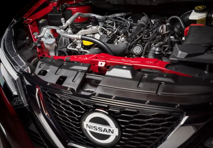 Silnik 1.6 benzyna w Nissan Qashqai. Czerwone elementy karoserii i skomplikowana sieć przewodów pod maską.