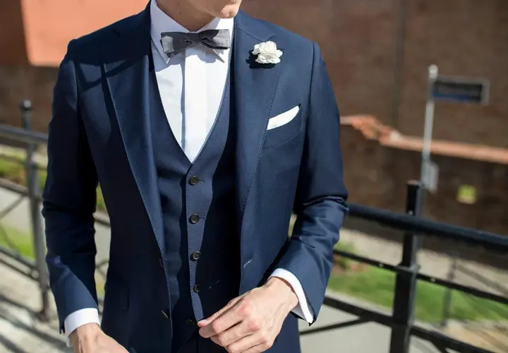 Eleganckie stylizacje z kamizelką pikowaną: granatowy garnitur, biała koszula, szara mucha i biała butonierka.