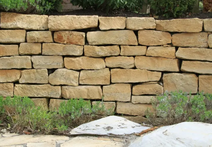 Eine rustikale Natursteinmauer bauen, die mit Lavendel und Steinen verziert ist.