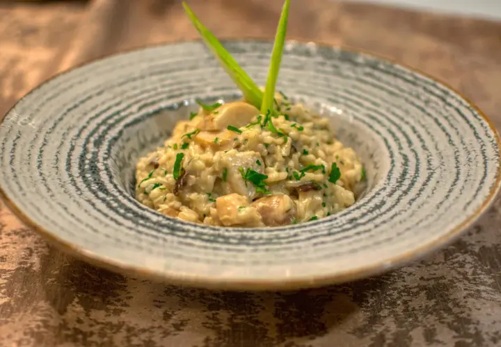 Kremowe risotto ze szparagami i grzybami, udekorowane zieloną cebulką i natką pietruszki, podane w ozdobnej misce.