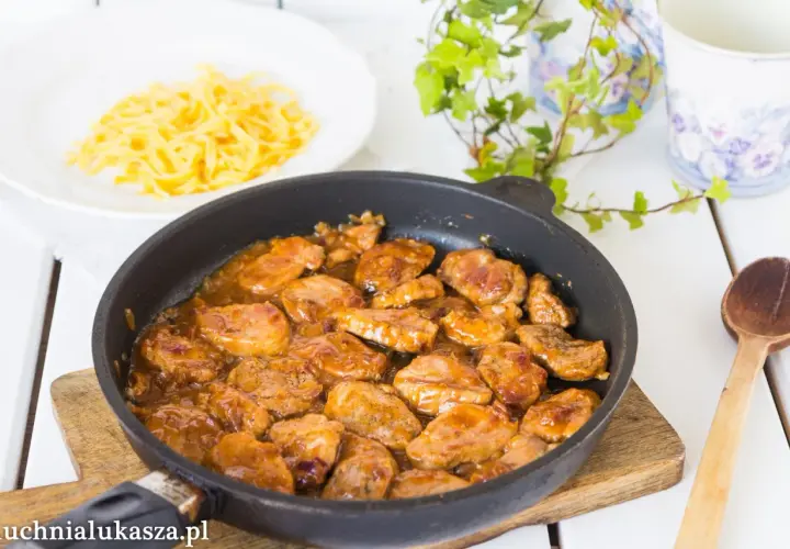 Polędwiczki w sosie miodowo musztardowym w patelni, obok talerz makaronu. Pyszne danie gotowe do podania.