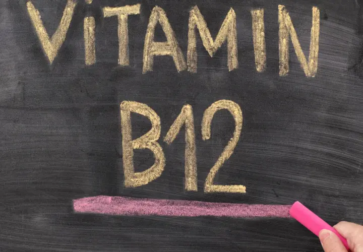 Kreidezeichnung "VITAMIN B12" auf einer Tafel, daneben eine Hand mit pinker Kreide.