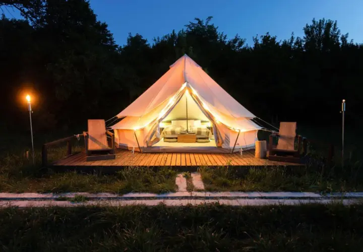 Tienda iluminada para camping Portugal, ideal para familias con niños. Dos sillas de madera esperan en la terraza.