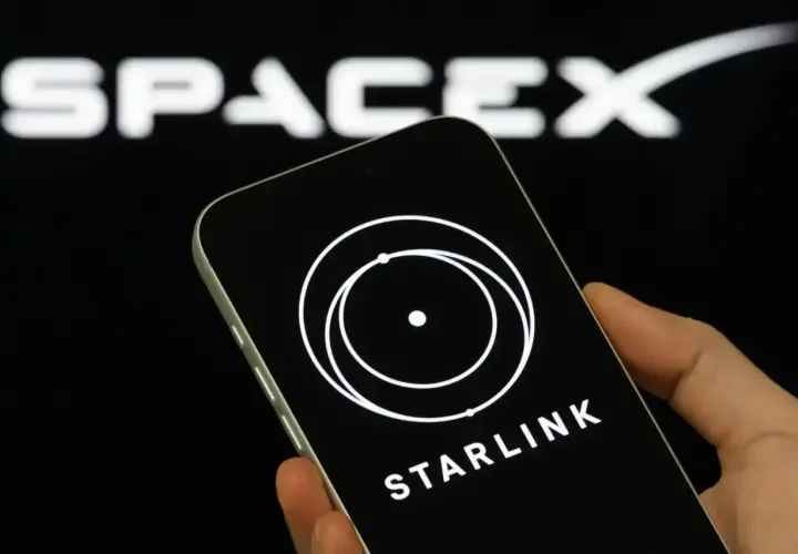 Dłoń trzyma smartfon z logo Starlink na ekranie, w tle logo SpaceX.