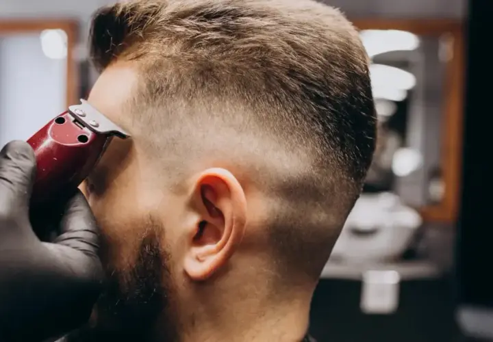 Barbero con guantes negros crea un corte de pelo **low fade** a un hombre con una máquina.