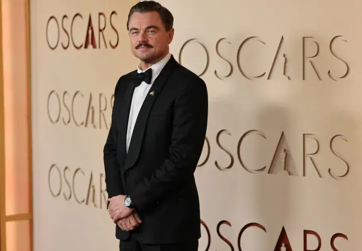 Leonardo DiCaprio w eleganckim smokingu pozuje na tle ścianki z napisem "OSCARS".