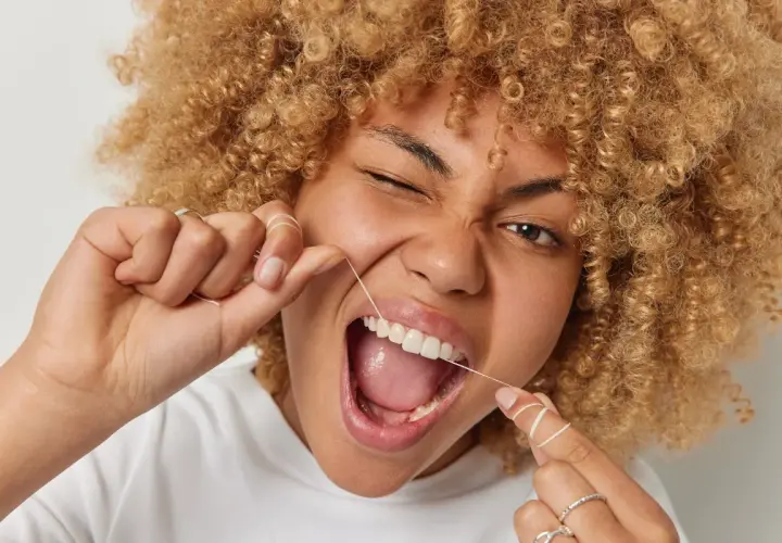Donna con capelli ricci usa il filo interdentale per una pulizia perfetta.