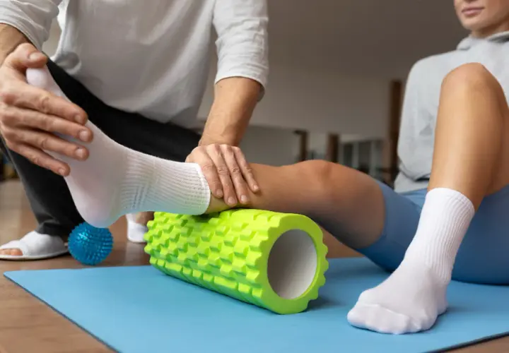 Fizjoterapeuta pomaga sportowcowi w automasażu łydki wałkiem, co jest kluczowe w klinicznej medycynie sportowej.