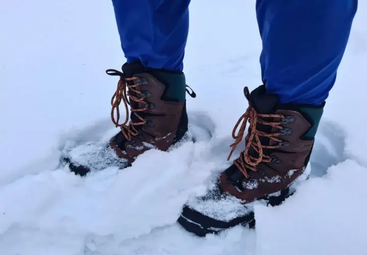 A person wearing blue pants and brown hiking boots stands in deep snow. These boots seem to be performing well, raising the question: can hiking boots be used as snow boots?