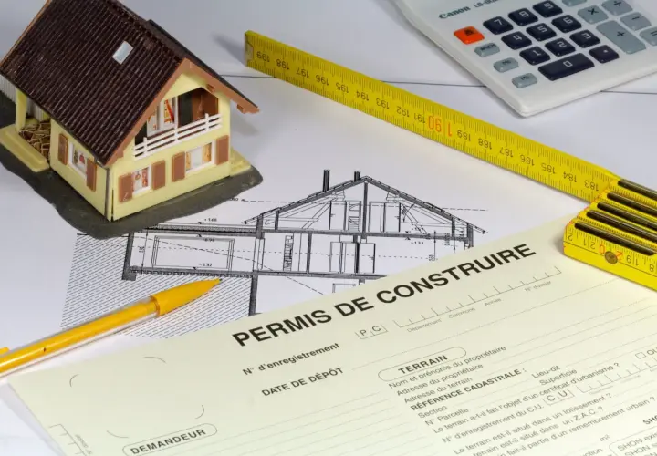 Maquette de maison, plans, mètre, calculatrice et formulaire "Permis de construire". La question : peut-on commencer les travaux pendant le recours des tiers ?