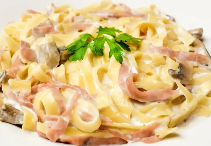 Pasta carbonara con setas y bacon, cremosa y deliciosa, coronada con perejil fresco.