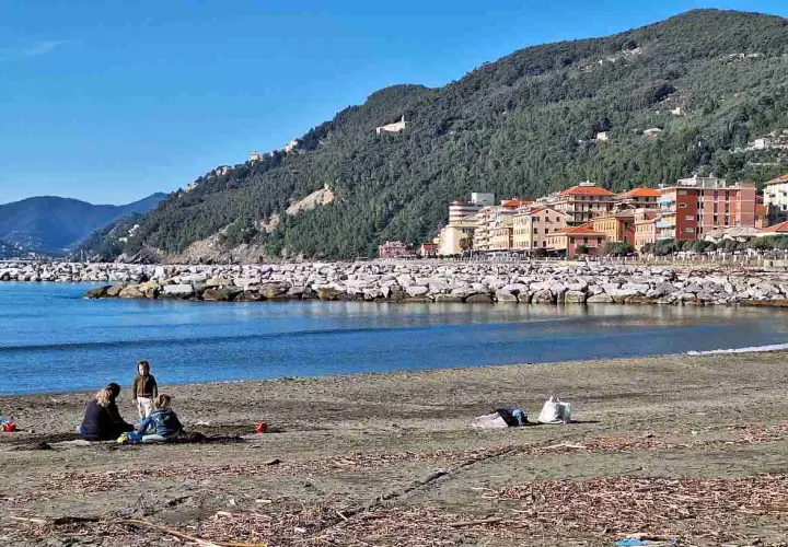 Vue de la plage de Chiavari avec des familles profitant du soleil, des bâtiments colorés et une colline verdoyante en arrière-plan.