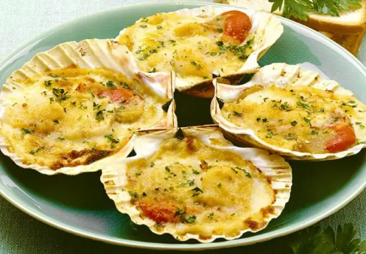 Quattro capesante gratinate, un delizioso antipasto di pesce, servite in conchiglia con erbe aromatiche.