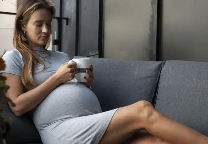 En gravid kvinna i sitt andra trimester vilar på en soffa med en kopp i handen.