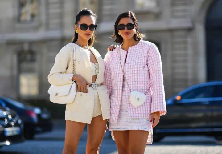 Dos mujeres lucen conjuntos de tweed, uno blanco y otro rosa, encarnando la moda preppy con bolsos a juego y gafas de sol.
