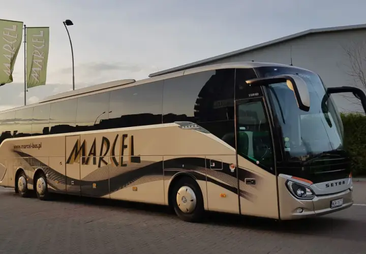Autobus Marcel z napisem na boku, stojący na parkingu, z zielonymi flagami w tle.