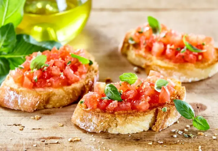 Trzy chrupiące kromki pieczywa, obficie posypane posiekanymi pomidorami i listkami bazylii. To klasyczna bruschetta włoska, gotowa do skropienia oliwą.