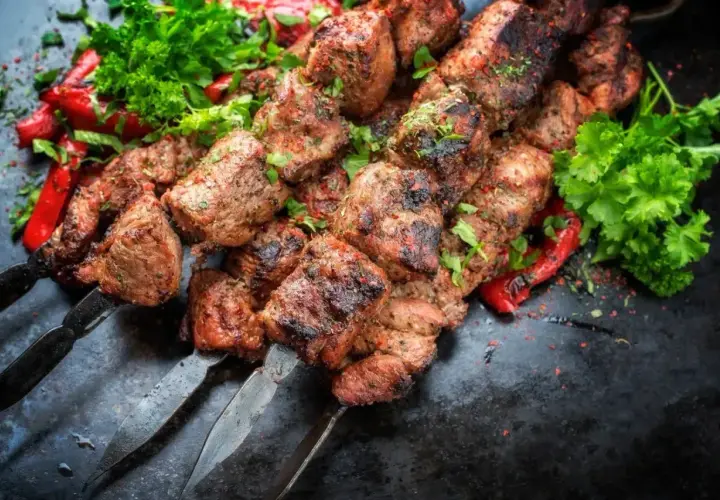 Soczyste kawałki kofta kebab na metalowych szpikulcach, ozdobione papryką i natką pietruszki.