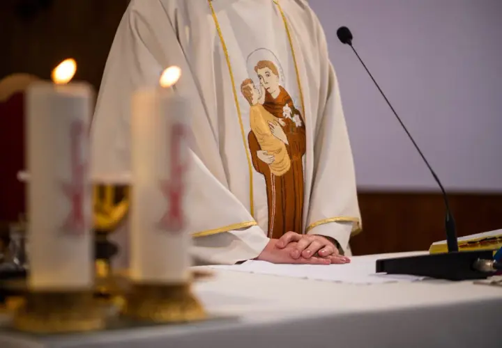 Szczegół szaty kapłańskiej z haftem świętego z dzieckiem, świece i mikrofon.