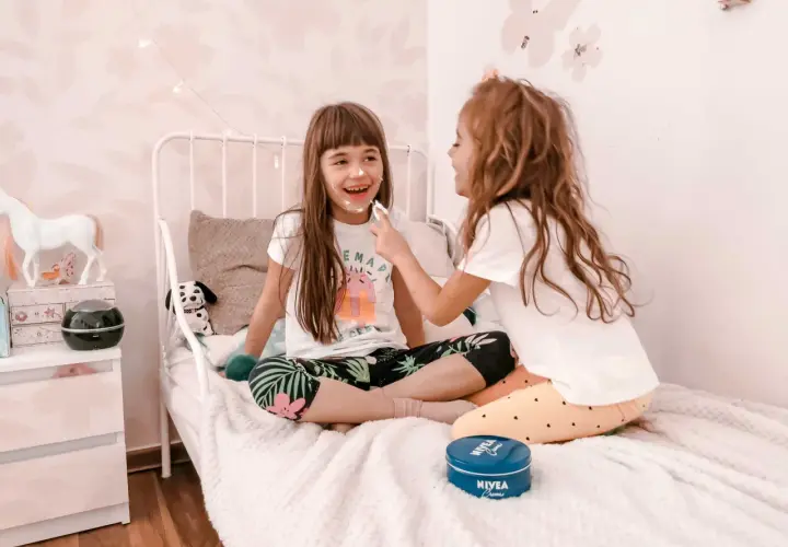 Dwie dziewczynki śmieją się, malując sobie nawzajem twarze kremem. To świetne zabawy dla 10 latków, pełne radości i kreatywności.