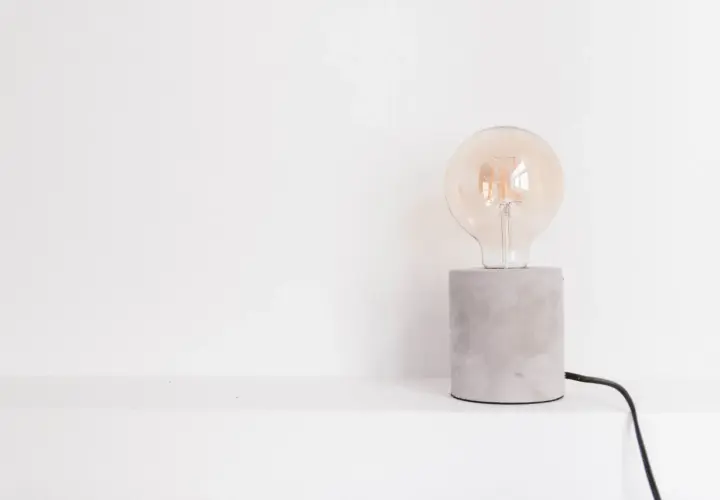 Bombilla Edison de cristal transparente sobre base de cemento gris con cable negro.