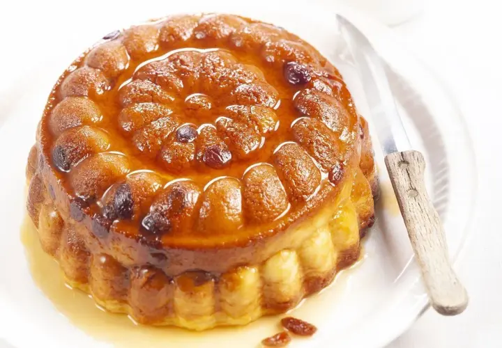 Gâteau de semoule doré et moelleux, nappé d'un sirop ambré et parsemé de raisins secs. Un couteau est posé à côté, prêt à découper cette gourmandise.