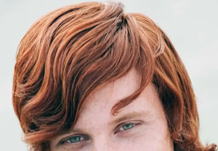 Ojos verdes y cabello pelirrojo ondulado, con pecas visibles en la piel.