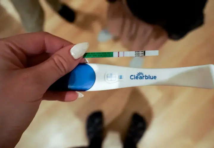 En hand håller upp ett positivt graviditetstest. Två streck syns på teststickan, vilket indikerar vilken vecka gravid.