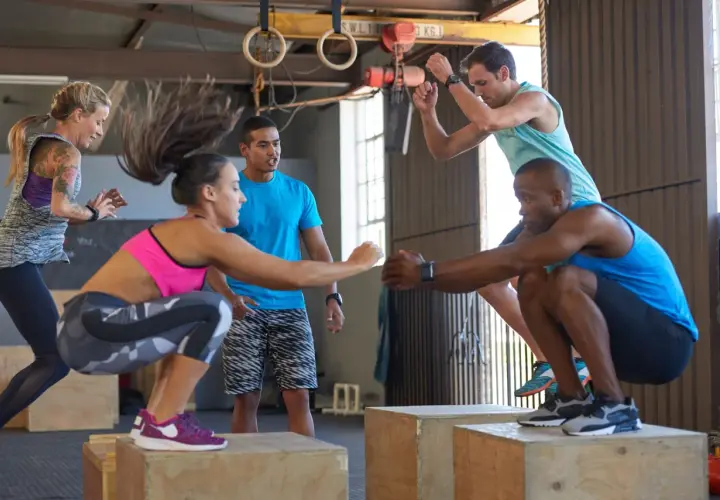 Grupa osób wykonująca ćwiczenia z wyskokami na skrzynie w sali treningowej CrossFit.