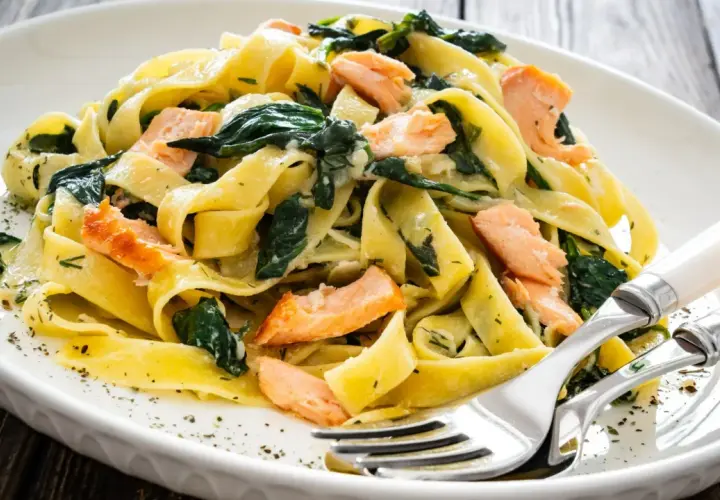 Pappardelle z łososiem i szpinakiem, danie fit, podane na białym talerzu z widelcem i nożem.