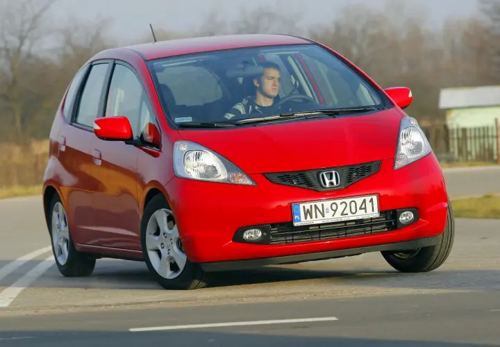 Czerwony Honda Jazz z młodym kierowcą za kierownicą. Wiele osób szuka honda jazz opinie przed zakupem.