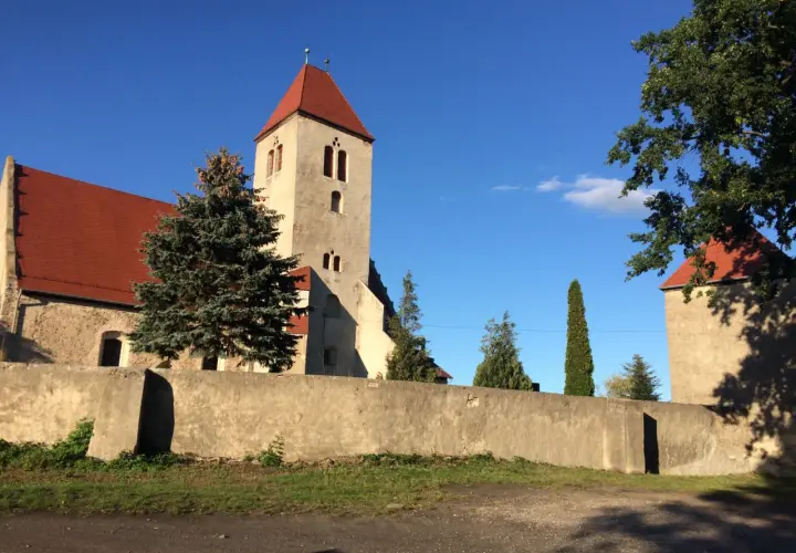 Kamienna wieża kościelna z czerwonym dachem w Nowogród Bobrzański, otoczona murem i zielenią.
