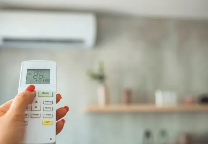 Mano con control remoto para cambiar temperatura aire acondicionado. Pantalla muestra 25°C.