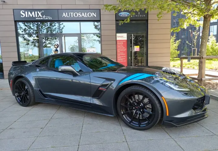 Szary Chevrolet Corvette C7 z niebieskimi pasami, zaparkowany przed salonem samochodowym. Sprawdź aktualną corvette c7 cena!