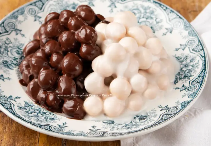 Pignolata messinese: palline dolci ricoperte di cioccolato fondente e glassa bianca, servite su un piatto decorato.