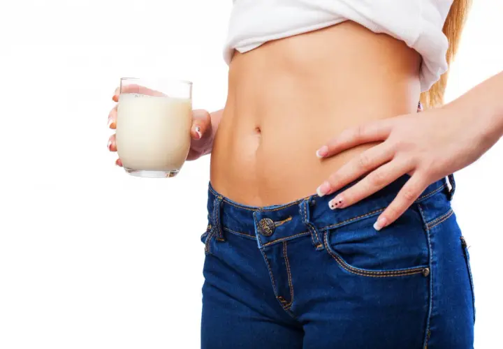 Donna con jeans e maglietta bianca tiene un bicchiere di latte. Un aiuto per capire cosa bere per andare in bagno velocemente.