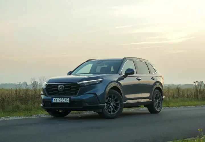 Ciemnoniebieski Honda CR-V Hybrid na tle zachodzącego słońca, zaparkowany na poboczu drogi.
