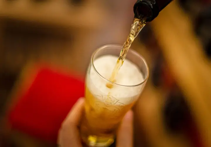 Z butelki leje się złociste piwo Peroni do szklanki, tworząc obfitą pianę.