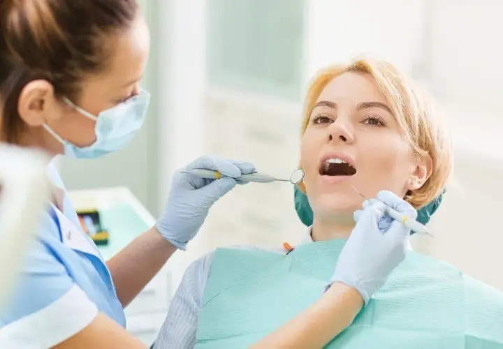 Dentystka bada zęby pacjentki narzędziami stomatologicznymi.