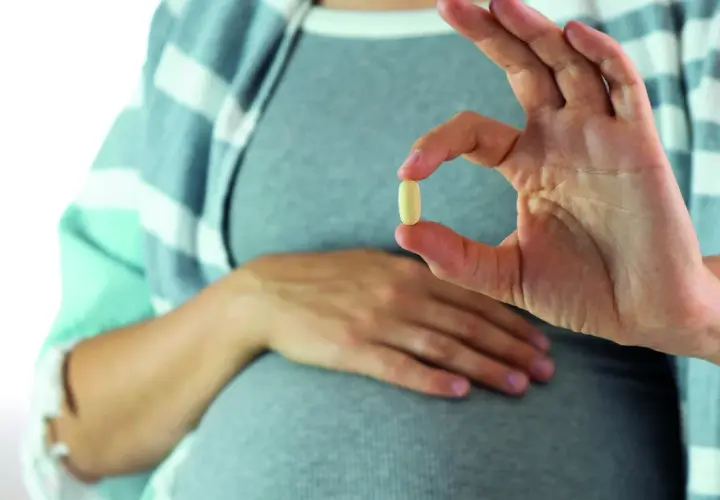 Mujer embarazada muestra una pastilla, una solución para saber como quitar acidez estomago.