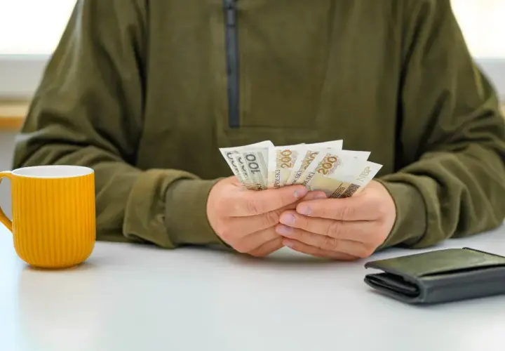 Osoba liczy pieniądze, być może czekając na podwyżki dla pracowników samorządowych. Obok stoi żółty kubek i portfel.