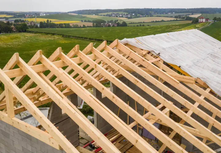 Charpente en bois sur un chantier, recouverte d'une bâche. La question est : combien de temps peut-on laisser une charpente dehors avant qu'elle ne se dégrade ?