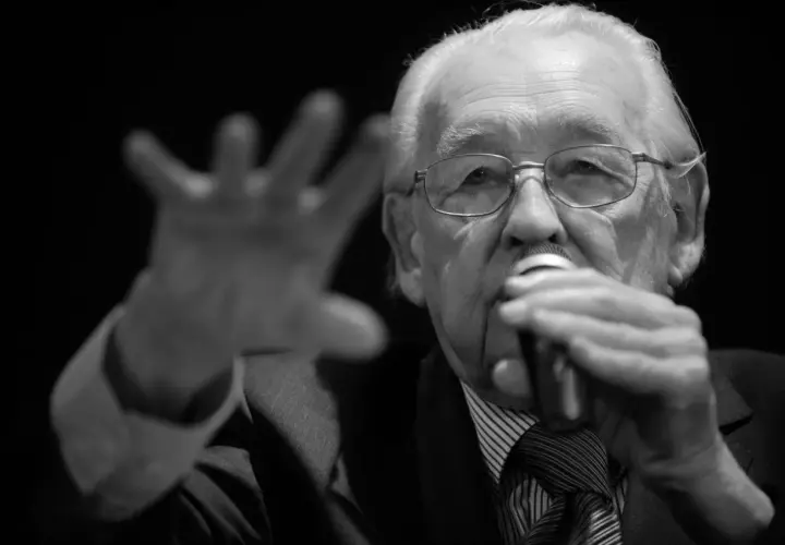 Portret starszego mężczyzny w okularach, trzymającego mikrofon. Wśród znanych reżyserów polskich, jego postać budzi szacunek.