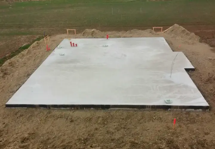 Nowa płyta fundamentowa gotowa na budowę domu. Widać wystające rury i elementy instalacji.